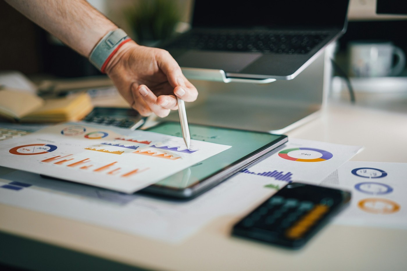 Hand with a stylus reviewing printed and on-screen marketing charts, representing an Amazon seller comparing Attribution report results by channel
