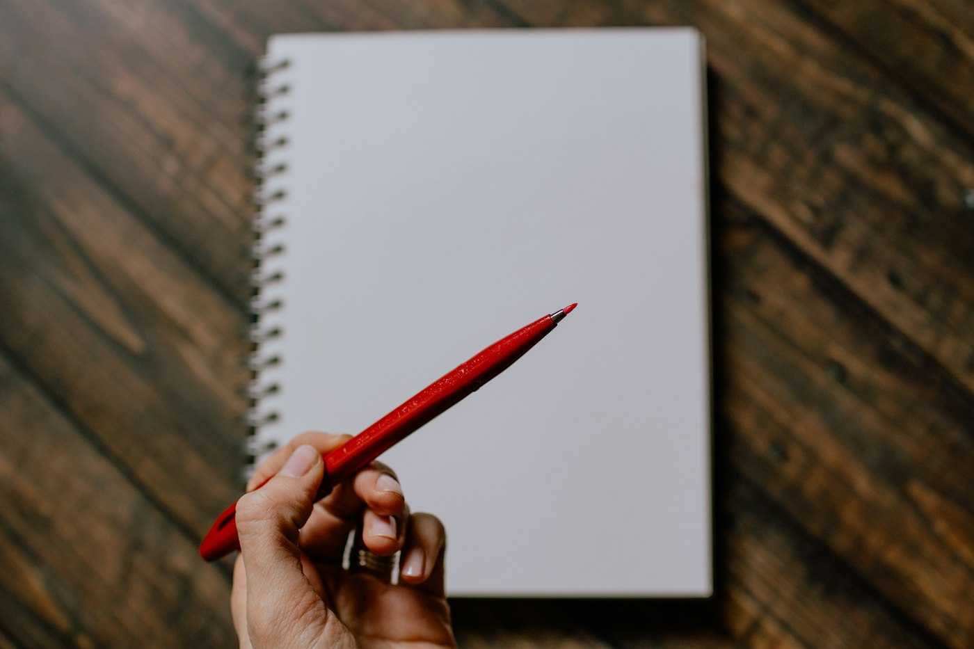 Hand holding a red pen over a blank notebook, ready to draft a shorter Amazon product title