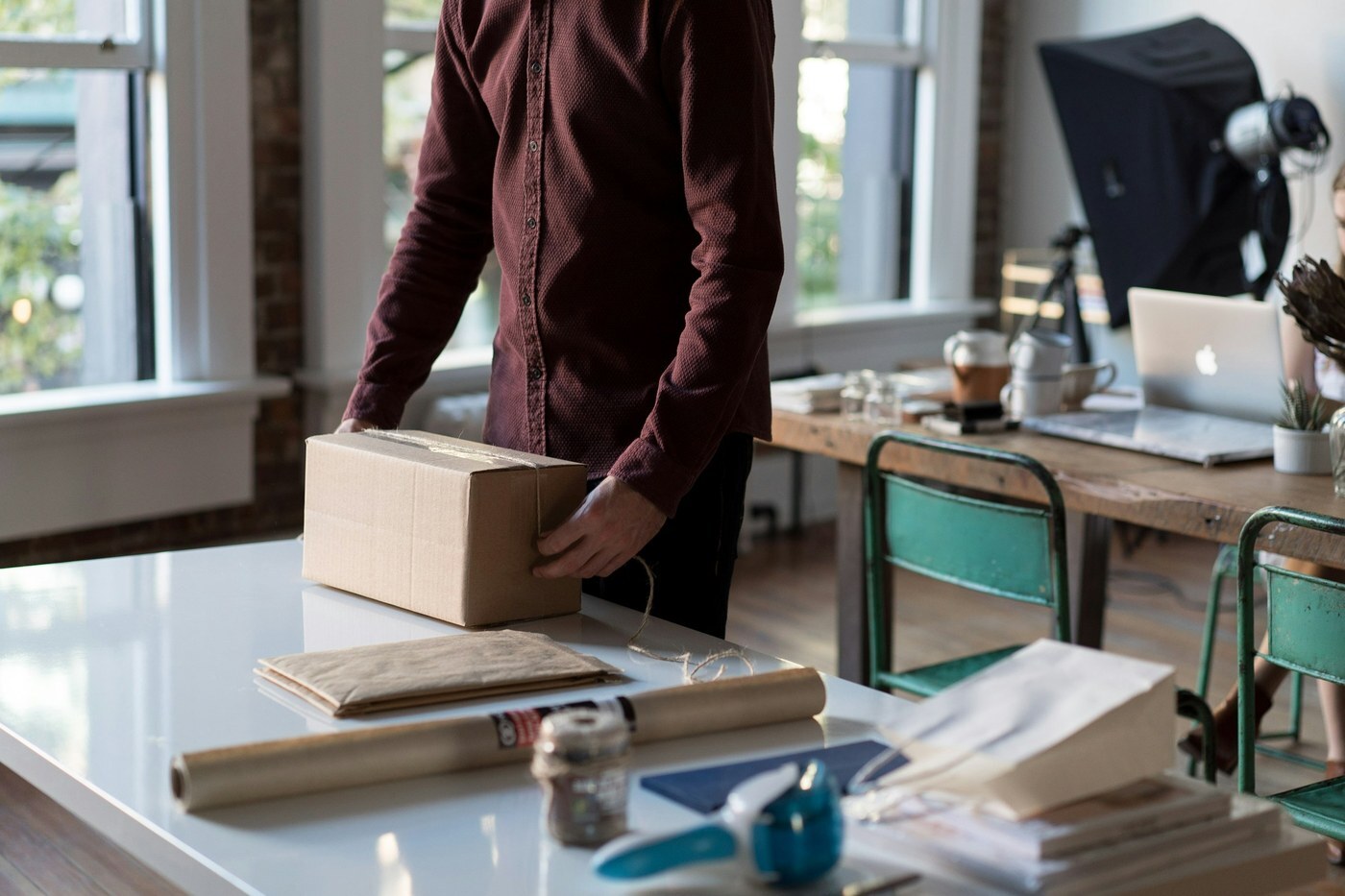 Person holding a sealed cardboard shipping box on a desk, representing an FBA customer return headed back to Amazon