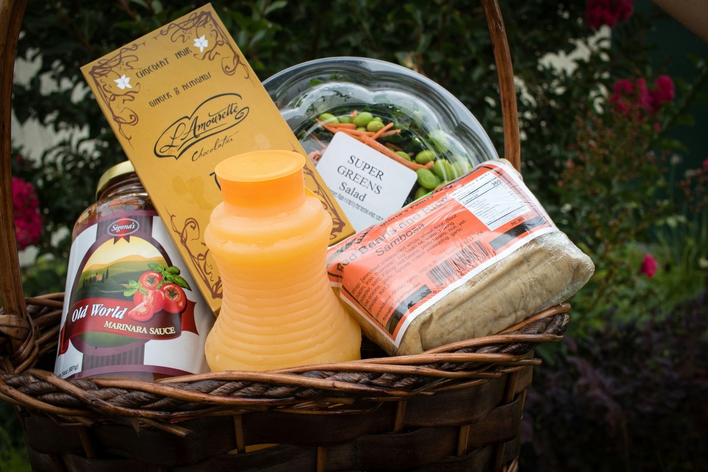 Wicker gift basket filled with marinara sauce, chocolate, juice, and snacks from different brands, an example of a multi-brand gift basket that falls under Amazon's gifting exception