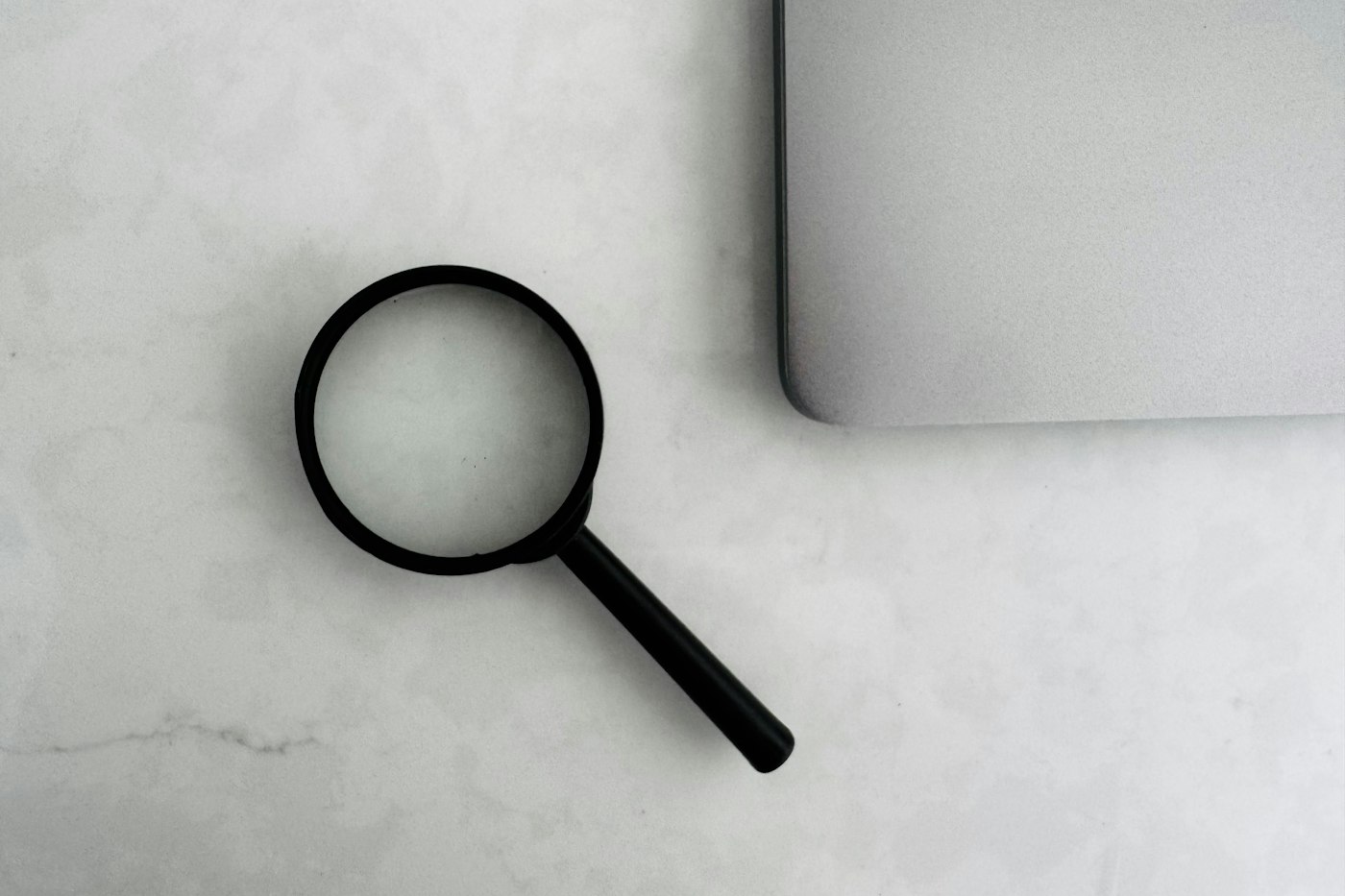 Magnifying glass next to a laptop, representing a weekly audit of FBA inventory and reimbursements