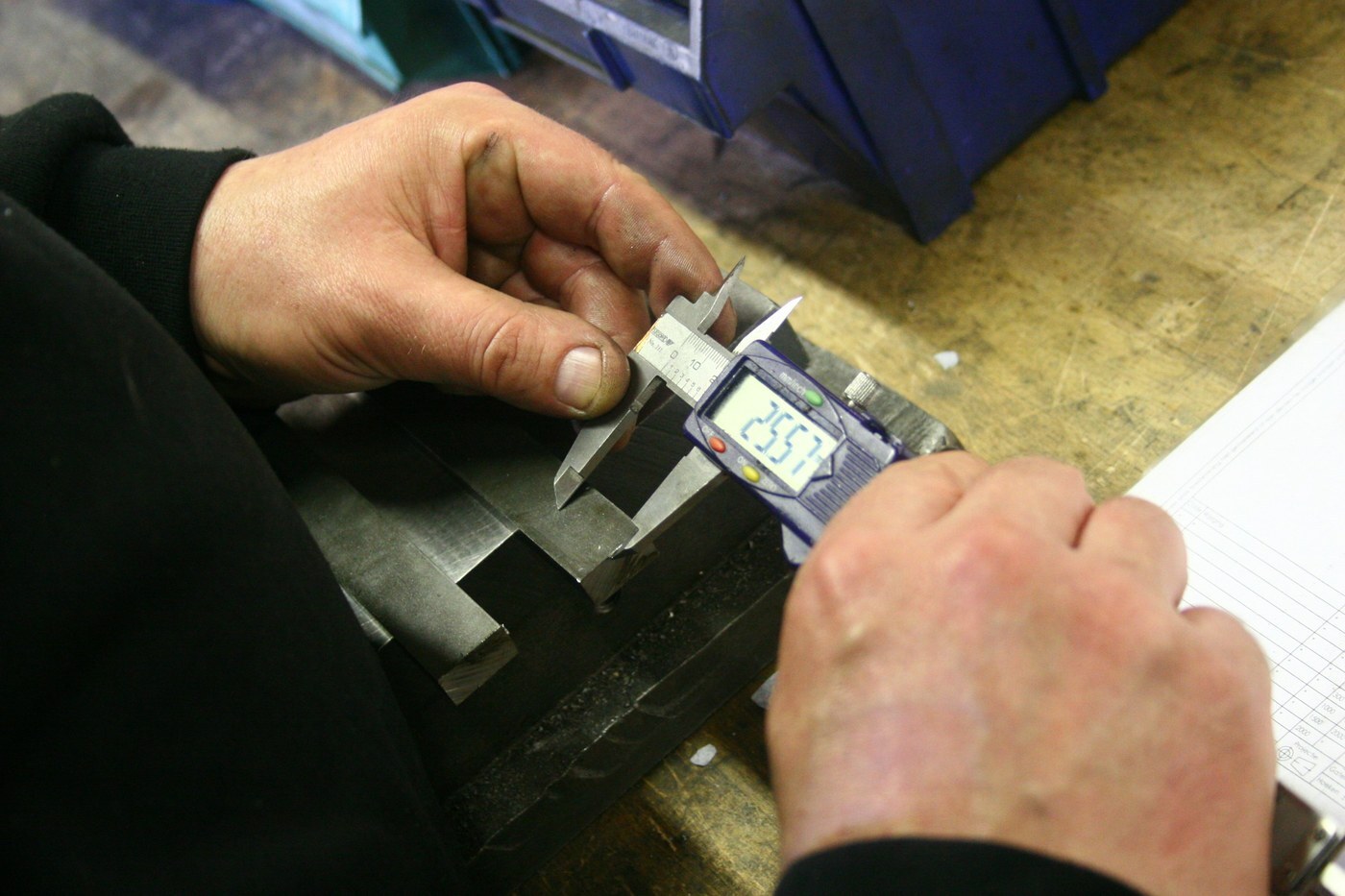 Hands measuring a metal part with a digital caliper, representing root-cause quality checks behind Amazon NCX and CX Health issues
