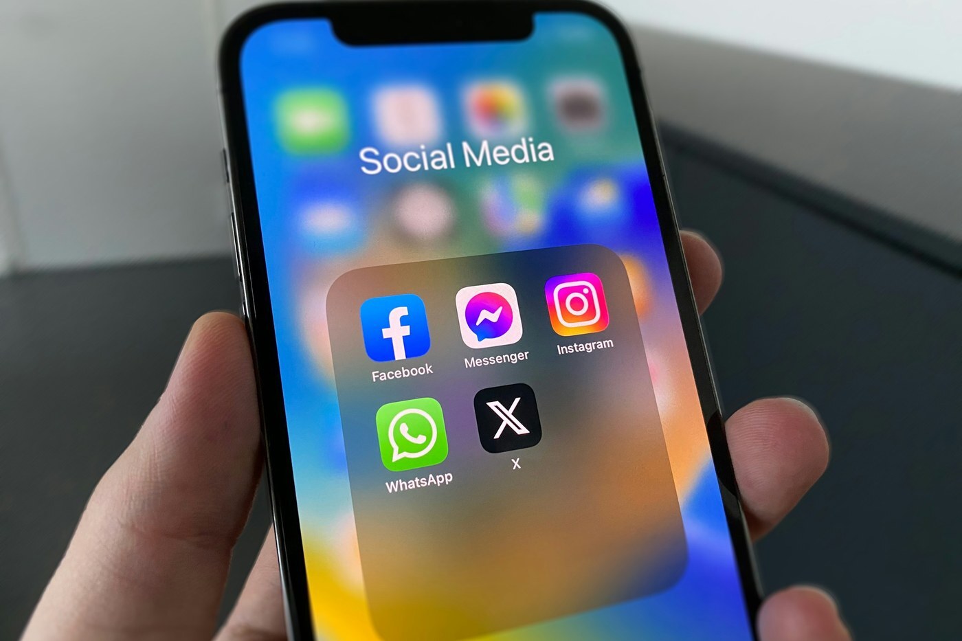 Hand holding a smartphone with a Social Media folder of Facebook, Messenger, Instagram, WhatsApp, and X apps, representing off-Amazon traffic that Amazon Attribution can track
