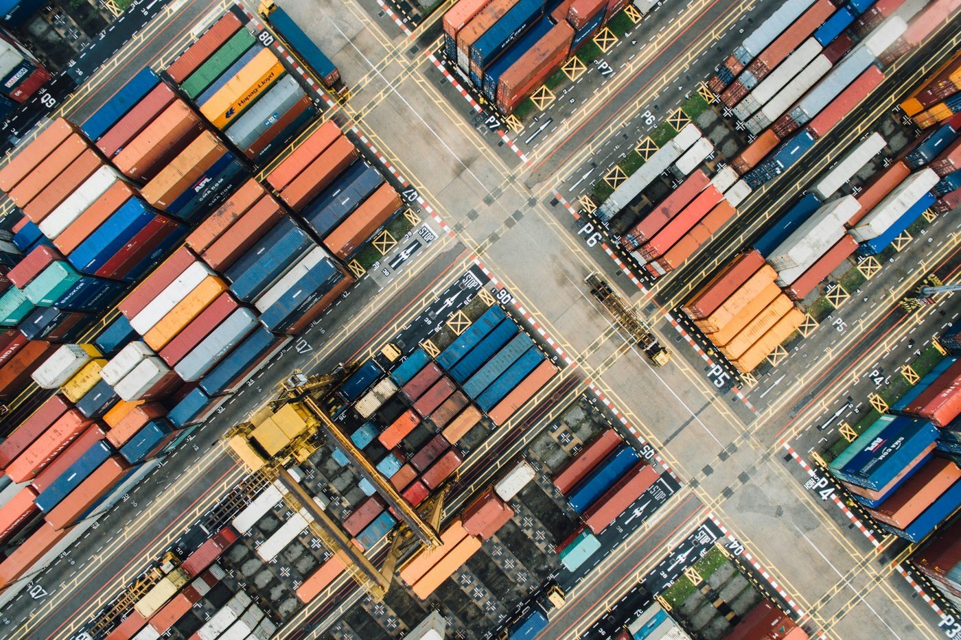 Aerial view of a shipping container yard with stacked colorful containers and a crane, representing Amazon FBA capacity limits and planning inventory space before peak season