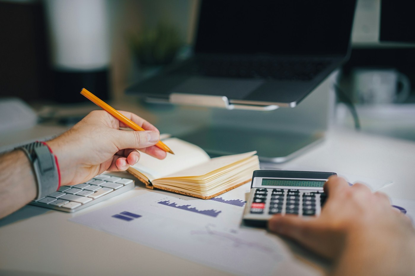 Hands with calculator and notebook over printed charts on a desk, representing Amazon seller planning for holiday peak fulfillment fees